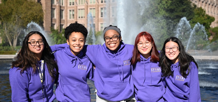 A group of students smiling in front of a campus fountain