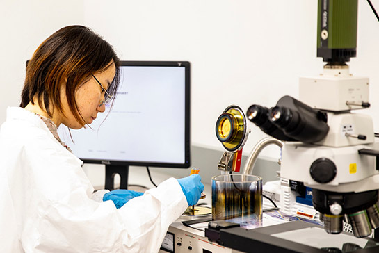 Student wearing lab coat and protective equipment working in materials science and engineering lab setting