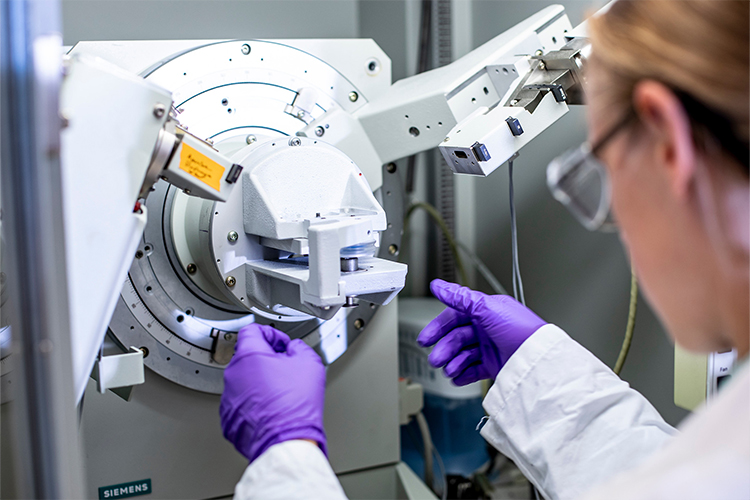 Fourth slide: Closeup of a woman wearing purple gloves and a white coat working on a machine