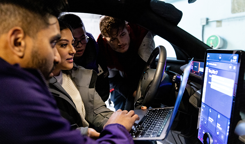 Team looking at a laptop screen inside a car as they work on an electric vehicle project for the industry capstone program