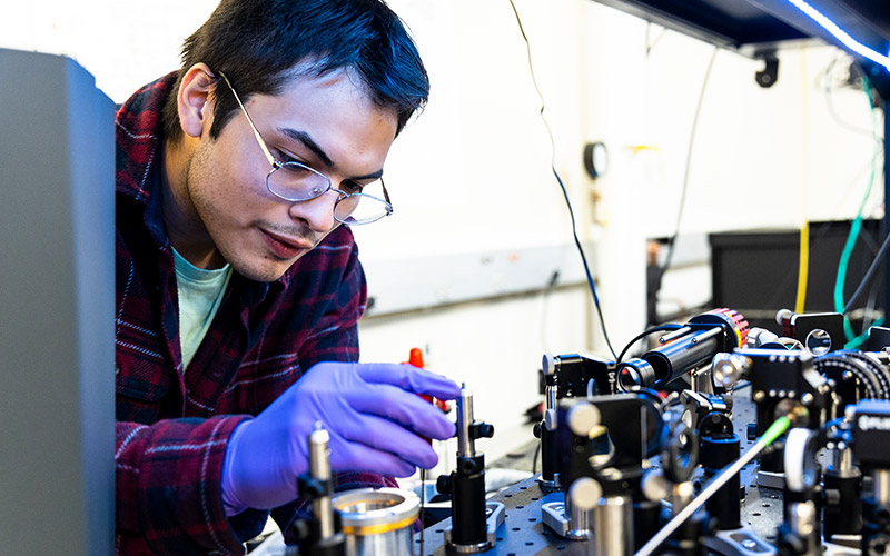 Undergraduate Enrique Garcia prepares to remove the diamond sample from the quantum processor, where it is mounted in a temperature-controlled cryostat.