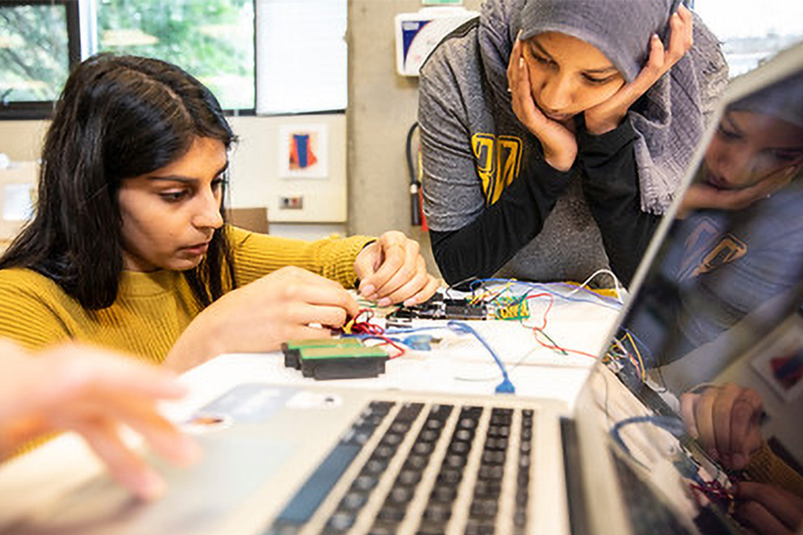 Two students studying a circuit board on a desk