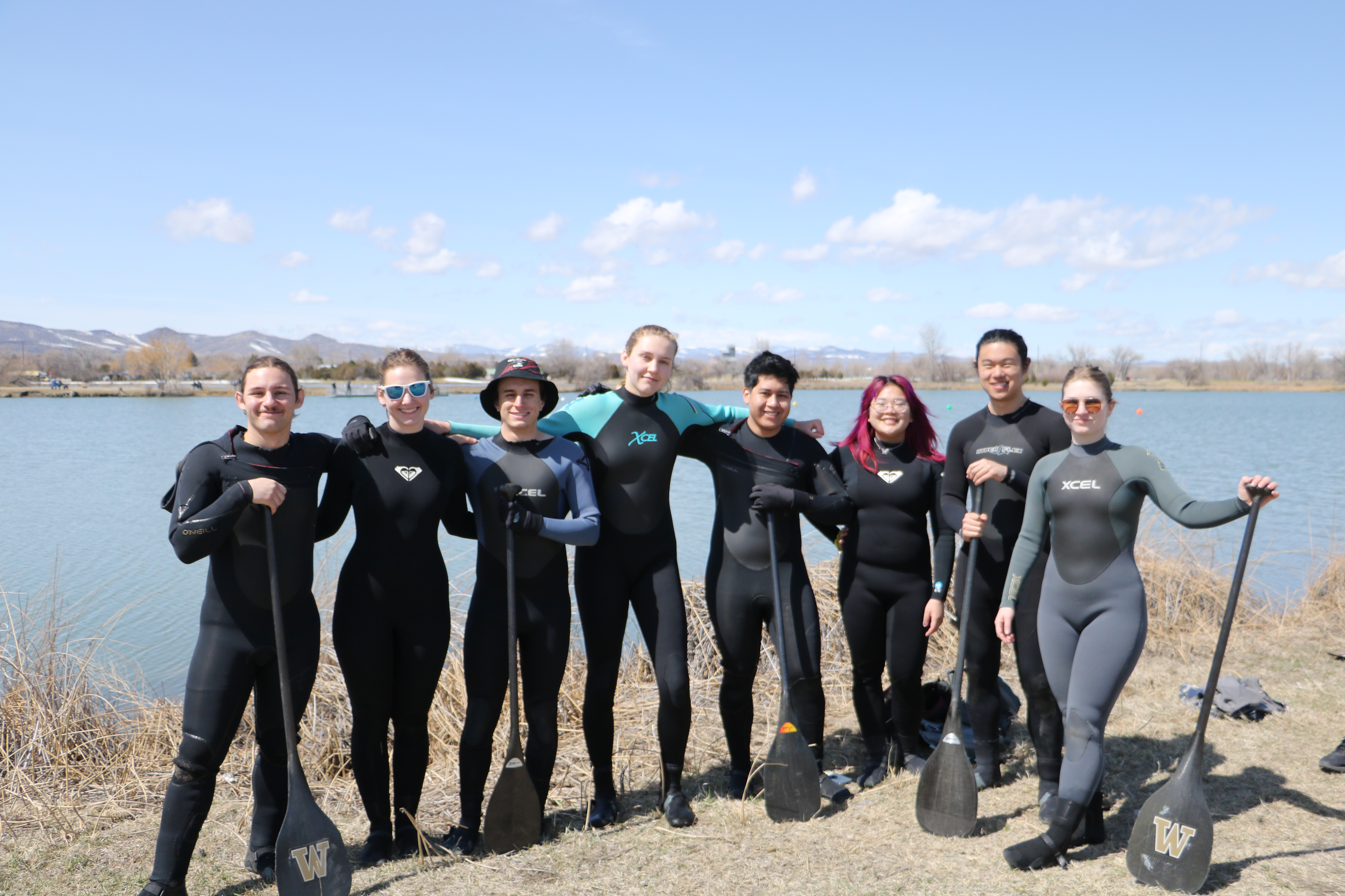 Holding canoe paddles, students stand near the water