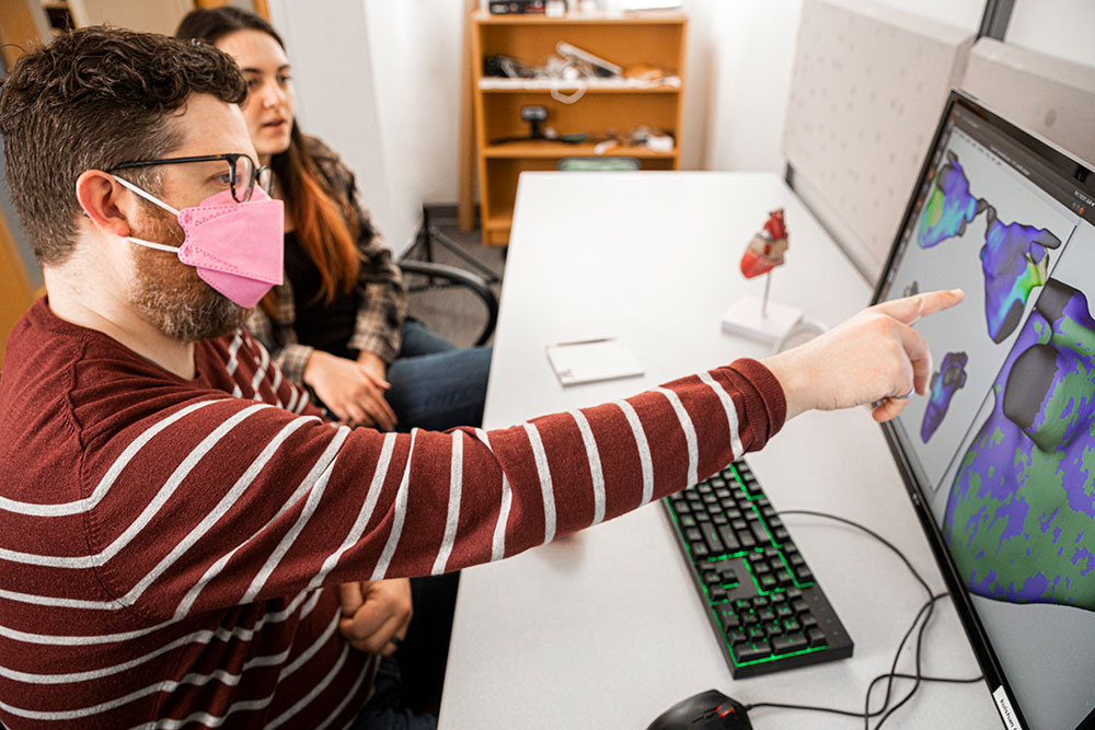 Boyle pointing at a computer monitor while sitting next to a student