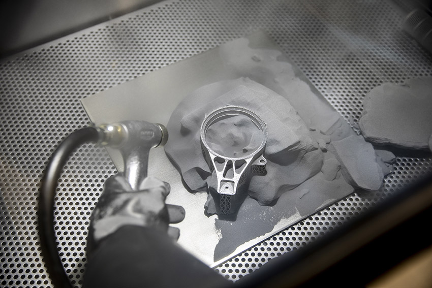 A lab engineer using a tool to blow titanium powder from the block