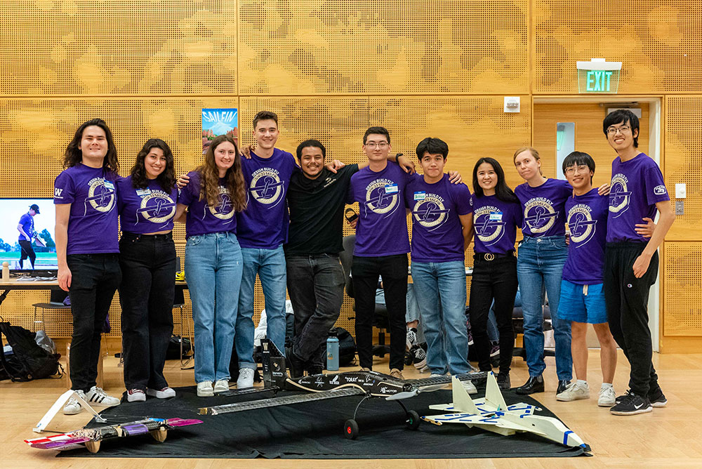 A group of students standing behind small aircrafts placed on the floor