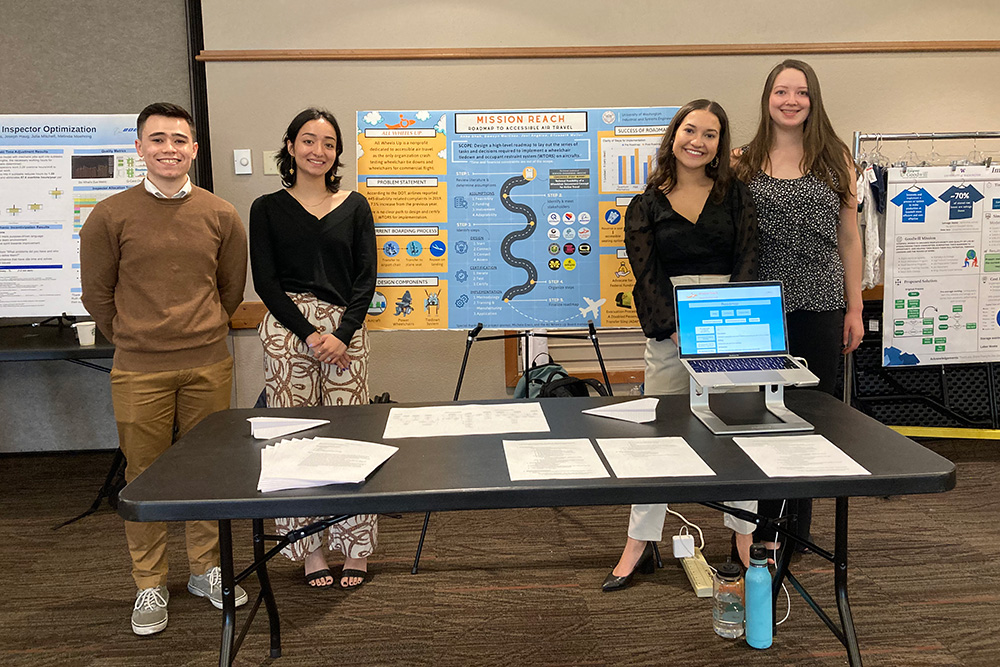 Four students standing in front of a large poster of their Capstone project