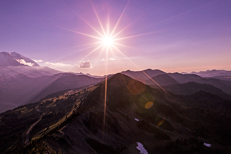 A bright sun illuminates a landscape photo of Mt Rainier