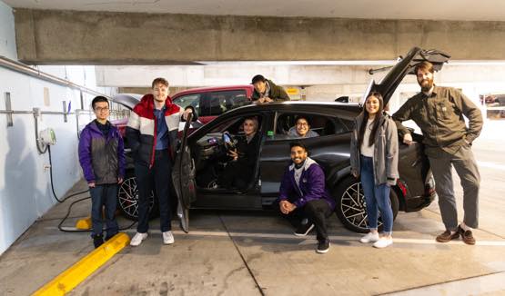 Students posing around an electric car