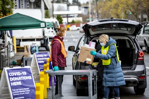 Woman gives a box of masks to a donation drive at a UW parking lot.