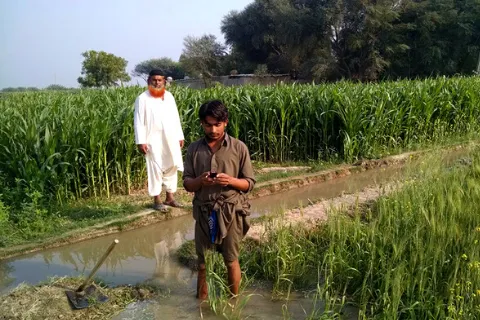 A Pakistani farmer standing in a farm field and looking down at this cell phone