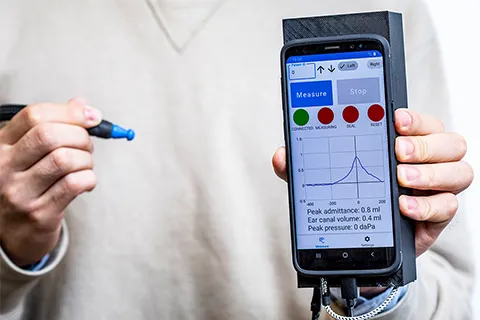 Closeup of person’s hands holding rubber-tipped ear canal probe and smartphone attached to 3D-printed casing. 