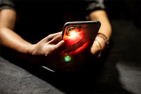 A hand holding a cellphone with one finger over the flash and the camera. The flash is shining through the finger and glowing red.
