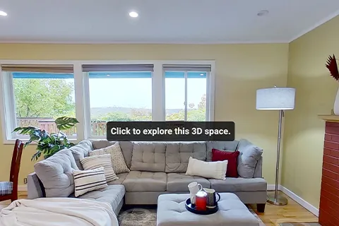 A screenshot of a virtual tour of a house. The scene is in a living room and there is a bar over the picture that says "click to explore this 3D space"