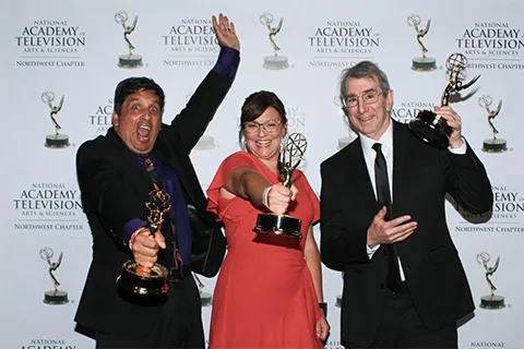 Three people holding Emmy awards and celebrating.