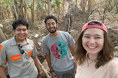 EWB members Alex Arevalo-Perez, Shoaib Laghari, and Kyra Dugan (left to right) stand in front of a trench they helped dig for electrical cables