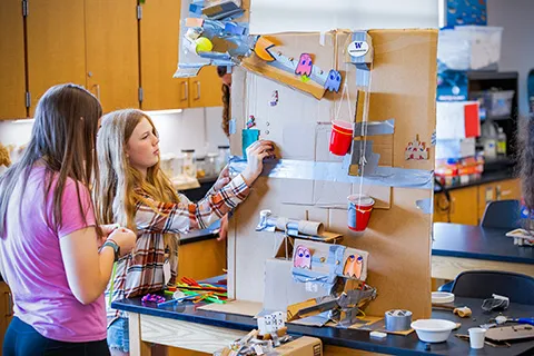 Two students work on their Rube-Goldberg inspired machine