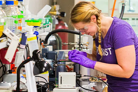 Woman working in a lab wearing purple gloves and goggles