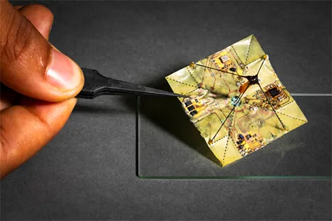A hand holding tweezers that are holding a yellow square with circuits on it