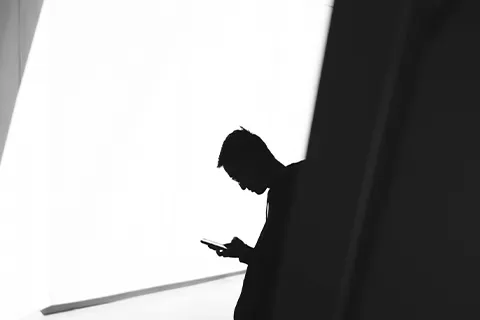 A silhouette of a person looking at a phone