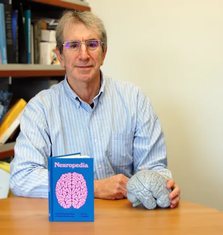 Man sitting at a table with a book and a model of a brain