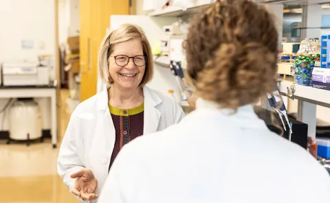 Mary Lidstrom smiling in lab while talking to student in lab coat