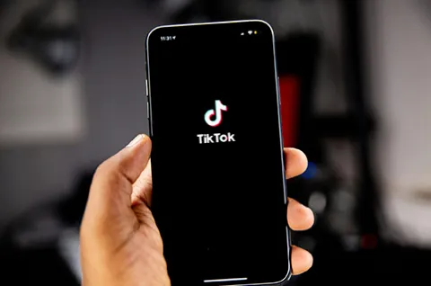 A hand holds a smartphone with the TikTok app open.
