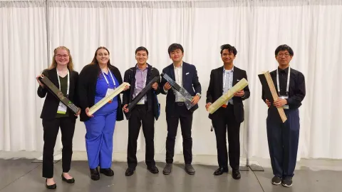 The 2023 team at the Conference Exhibition holding their competition beams.