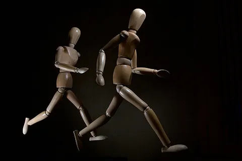 Two wooden artist's models placed in running motion, side-by-side in front of a dark background