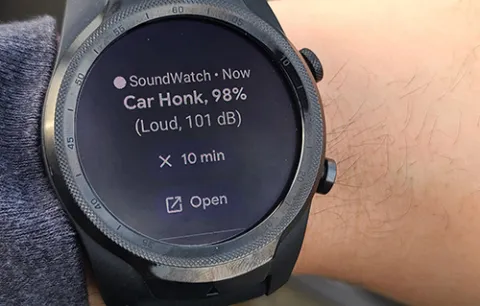 A wrist with a smartwatch on it. The smartwatch has an alert that says "Car honk, 98%, Loud, 101 dB" It also has options to snooze the alert for 10 minutes or open in an app on the user's phone