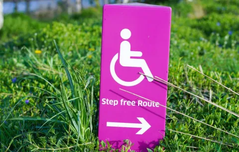 a sign in the grass with an icon of a wheechair user