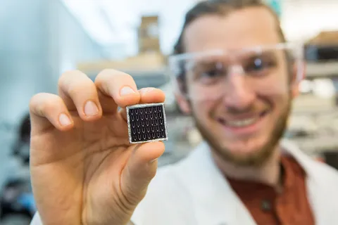 A person standing in a laboratory holding up a small solar cell