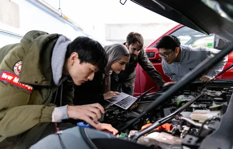 Four people inspecting the motor of an electric vehicle 