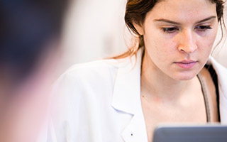 Student wearing lab coat looking at laptop screen